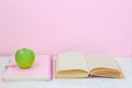 Apple, book, copybook on the desk on pink background