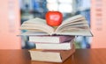 An apple on the books on the table with bookshelf in the library bookshelves background - Education learning concept open book