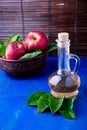 Apple cider vinegar in glass bottle on blue background. Red apples in brown bowl. Royalty Free Stock Photo