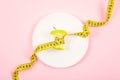 Apple core with measuring tape in place of the waist on a white plate on pink background. Diet, weigh loss, starvation, fitness