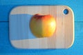 Apple cuted in half on a wooden board on turquoise table with a long blue shadow