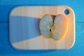 Apple cuted in half on a wooden board on turquoise table with a long blue shadow