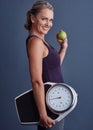 An apple a day...Studio portrait of an attractive mature woman holding an apple and a weightscale against a blue Royalty Free Stock Photo