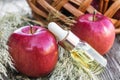 Apple essential oil on a wooden table near ripe red apples. Essential oil is used to fill lamps, perfumes and in cosmetics