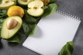 Apple halves, avocado with a stone, whole yellow lemons, ripe green spinach leaves, a blank sheet of Notepad on a gray