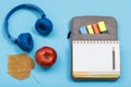 Apple, headphones, dry leaf, open exercise book on bag-pencil case with color felt pens and marker on blue background Royalty Free Stock Photo