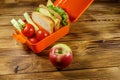 Apple and lunch box with sandwiches and fresh vegetables on wooden table