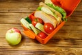 Apple and lunch box with sandwiches and fresh vegetables on a wooden table