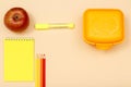 Apple, notebook, color pencils, felt pen and lunch box on beige background Royalty Free Stock Photo