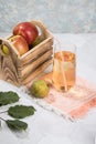 Apple and pear juice in a glass glass, apples in a wooden box on a light background.