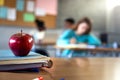 Apple and a pile of books and pens on teacher table in classroom. Focus on foreground.