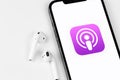 Apple Podcasts icon app on screen iPhone with AirPods headphones closeup