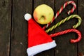 An Apple, red Santa hat, three candy cane lollipops on dark brown background Royalty Free Stock Photo