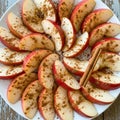 Apple slices with red skins are arranged in a circular pattern on a white plate, dusted with ground Royalty Free Stock Photo