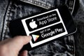 Apple Store and Google Play marketplaces icons, logo on iPhone 11 screen with black and white denim background