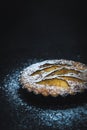 Apple tartlet on a black table, sprinkled with powdered sugar