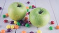 Apples and candies on a white wooden table. Harmful and healthy food on a white background.