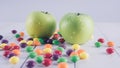 Apples and candies on a white wooden table. Harmful and healthy food on a white background.