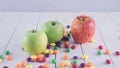 Apples and candies on a white wooden table. Harmful and healthy food on a white background.