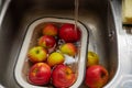 Apples in an enamel bowl under the flow water from tap in the sink Royalty Free Stock Photo