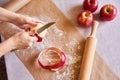 Apples, rolling pin, flour, parchment paper on the table. Woman`s hands peeling an apple. Preparation for cooking pastry Royalty Free Stock Photo