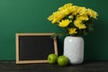 Apples, vase flowers and empty frame on green background, space for text Royalty Free Stock Photo