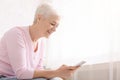 Positive retired lady using modern smartphone at home