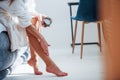 Applies cream on feet. Cropped photo of woman in white clothes that sits on the bed in room. Nice lighting