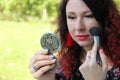 Applying foundation powder or blush with makeup brush. woman with red curly hair corrects her make-up on the green lawn Royalty Free Stock Photo