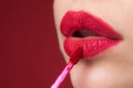 Applying lipstick, macro. Painting lips with bright lipstick, close up. Pampering, lips correction concept. Glossy