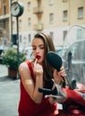Applying makeup on the street. fashion girl with red lips put lipstick looking in a mirror of motorcycle. Royalty Free Stock Photo