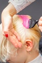 Applying pink dye with the brush on the white hair of a young blonde woman in a hairdresser salon. Royalty Free Stock Photo