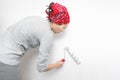 Woman applying primer and glue with a wide roller on the plastered surface of the wall for wallpapering