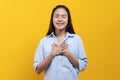 Appreciated expression. Pleased asian woman keeping hands on chest and closing her eyes isolated on yellow background studio shot Royalty Free Stock Photo