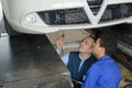 Apprentice mechanic working underneath car with professor