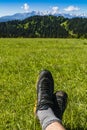 Approach shoes on the feet of a tourist resting during a trip on green grass in a clearing with a view of the mountain ridge Royalty Free Stock Photo