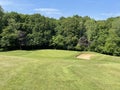 A downhill golf hole with a green and bunker backed by trees and blue sky Royalty Free Stock Photo