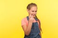 Approach to me! Portrait of cheerful cunning little girl with braid in denim overalls gesturing come here