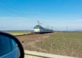 Approaching train and part of side view mirror of car standing in front of level crossing Royalty Free Stock Photo