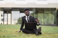 African businessman sitting on green grass outside office, showing thumb up while using laptop Royalty Free Stock Photo