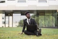 African businessman sitting on green grass outside office, showing thumb up while using laptop Royalty Free Stock Photo