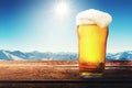 apres ski - cold beer glass on the table with sunny winter mountains landscape at ski resort