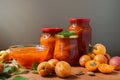 Apricot jam in a plate and glass jars. Fresh apricots fruit with leaves on table background