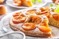 Apricot pie on a white plate, apricots, mint and powdered sugar on the kitchen table