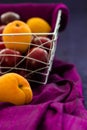 Apricots and plums in a wire basket with draped purple silk against a blue silk background with copy space