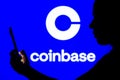 April 12, 2022, Brazil. In this photo illustration, a woman`s silhouette holds a smartphone with the Coinbase logo in the