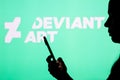 April 12, 2022, Brazil. In this photo illustration, a woman`s silhouette holds a smartphone with the DeviantArt logo in the