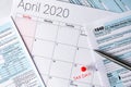 April 2020 calendar with the 15th pinned with tax day text, and 1040 tax forms