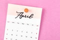 A April 2023 calendar and wooden push pin on pink colour background