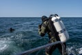 A scuba diver enters the water. Giant stride enter. Twin set tank. Ocean and blue sky in the background